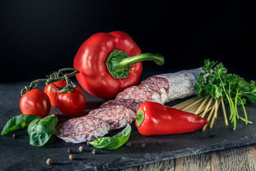 Salami with red paprika, tomatos  and pepper on the slate board