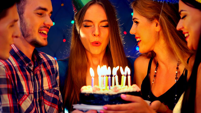 Happy friends birthday celebrating food with celebration cakes. Meet people wear in hat party blow out candles at burning candles. Women and men have fun in nightclub.Youth shout surprise together.