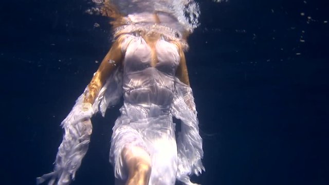 Underwater model in angel costume poses for camera in the Red Sea. Filming a movie. Young girl smiling. Extreme sport in marine landscape, coral reefs, ocean inhabitants.