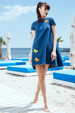 Model in jeans dress with butterfly print standing on the beach