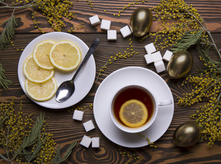 Easter eggs, cup of tea with lemon on a wooden background with flowers