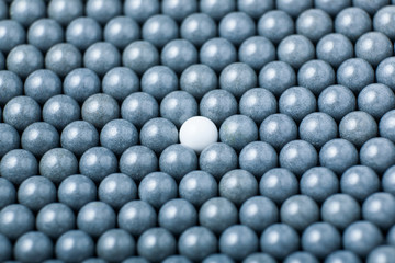 White airsoft ball is among many black balls. Background of 6mm bbs