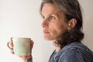 Profile view of natural looking middle aged woman looking thoughtful with green mug (selective focus)