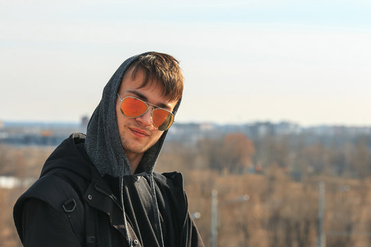 A handsome young white guy in sunglasses and in the hood on a sunny day.