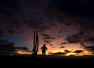 Silhouette of a woman standing next to a tall Cacti at sunset in the Tatacoa desert.