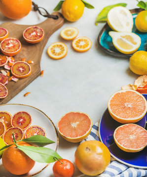 Natural fresh citrus fruits in colorful ceramic plates and wooden rustic cutting board over grey marble table background, selective focus, copy space