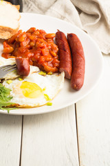 Fried eggs, beans, sausages and bread close-up on white wooden background background.
