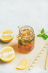 Summer cold Iced tea with fresh bergamot, mint and lemon in glass jar with splashes on light table background, copy space. Food in motion concept
