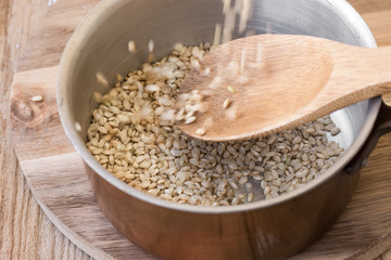 Pouring whole grain brown rice into copper pot on wooden spoon, motion, top view, close up