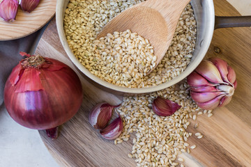 Whole grain brown rice uncooked in pot, onions garlic, wood spoon, meal ingredients, kitchen, top view