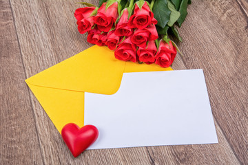 Yellow envelope, roses, heart and paper leaf on a wooden background