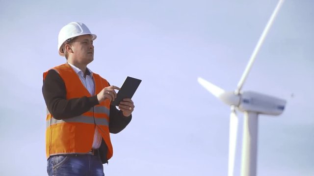 Energy Engineer of the windmill to work with the tablet at sunset. environmental