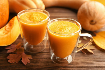 Two glasses with smoothies and fresh pumpkin on wooden background