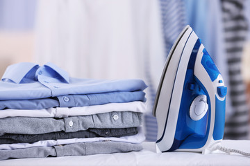 Electric iron and pile of clothes on blurred background