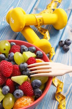 Fresh fruit salad with fork and centimeter with dumbbells, healthy lifestyle and nutrition concept