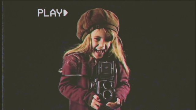Fake VHS tape: a cute little girl acting as a paparazzo (a stereotyped celebrities' photographer) with a vintage film camera.
