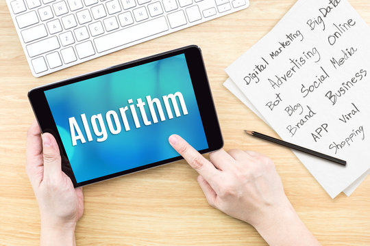 Hand using tablet with Algorithm word on screen with list of digital marketing features on paper on work table,Online business concept