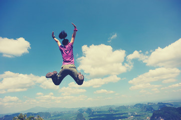 cheering successful young woman jumping on mountain peak