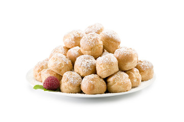 Pile of cream puffs on white plate with raspberry and mint with powdered sugar