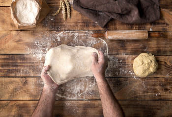 Male hand preparing pizza dough on the wooden table
