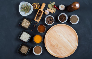 Obraz na płótnie Canvas Indian spices, herbs and empty round cutting board on black background