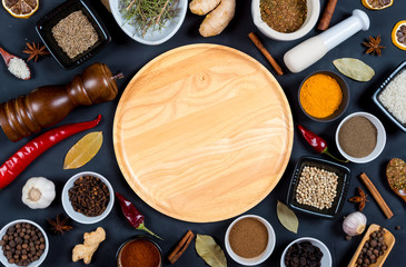 Indian spices, herbs and empty round cutting board on black background