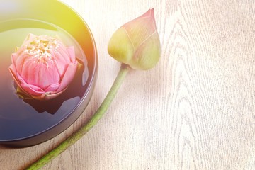 Pink lotus flower floating in water and wooden background, spa concept. Blurry lilies and artificial light and copy space. Technical Writing Property artificial light.