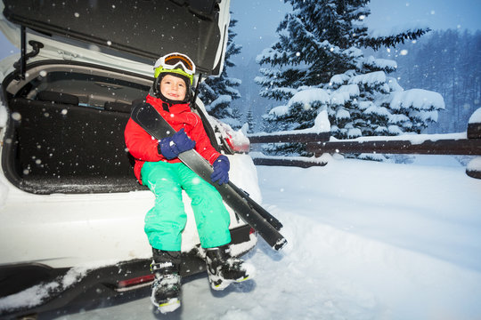 Boy skier sitting in the car trunk during snowfall