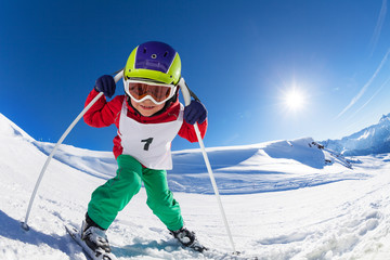 Cute little skier posing with poles at sunny day