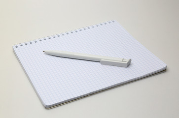 Блокнот в клеточку на пружине с белой шариковой ручкой на сером фоне