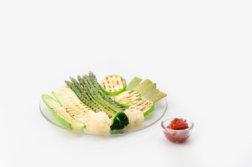 Grilled zucchini and asparagus, broccoli, lobi and cauliflower on a glass plate with red sauce