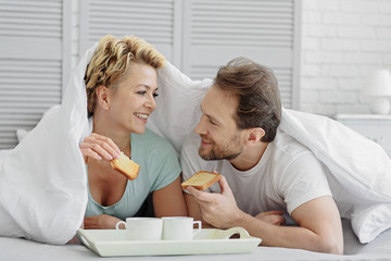 Happy man and woman enjoying breakfast on bedding