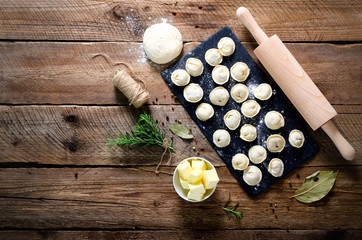 Ingredients for making pelmeni, ravioli, dumplings - dough, rosemary, rolling pin, canvas thread, butter, bay leaf. Top view. Wooden background