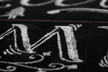 Closeup of calligraphy letter M drawn with chalk. Shallow depth of field.