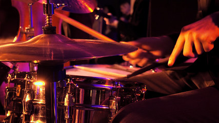 Drummer plays on drum set and cymbal with drumsticks on the stage. Jazz or rock concert performance entertainment. Close up shot with soft selective focus. - obrazy, fototapety, plakaty