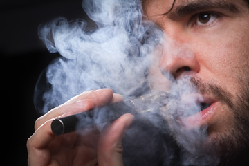 Young man smoking electronic cigarette on black background