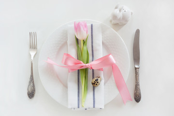 Easter table setting with pink ribbon and tulip on white background. Spring romantic dinner. Top view.