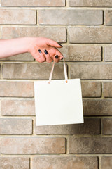 white shopping bag in female hand on brick wall