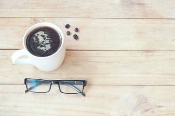 glasses near white cup coffee and coffee bean on wood