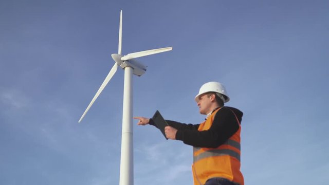 Energy Engineer of the windmill to work with the tablet at sunset. environmental