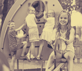 Fototapeta na wymiar Smiling girl sitting on swing on children's playground