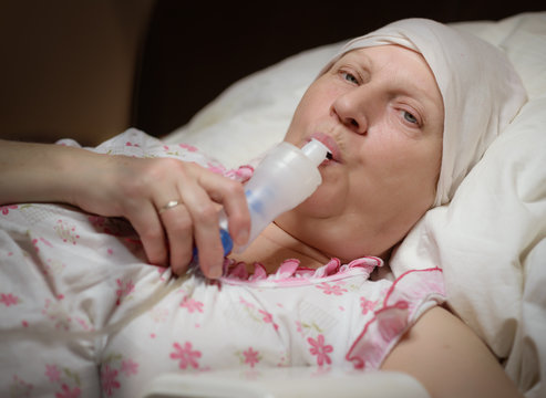 Aged woman is treated at home by breathing through a nebulizer.