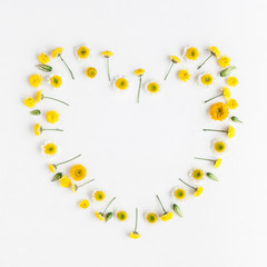 Flowers composition. Heart symbol made of various yellow flowers on white background. Flat lay, top view