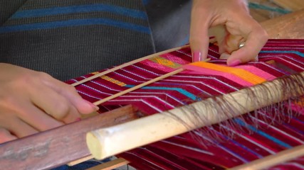 Balinese artist weaves colorful patterns using a traditional, wooden loom