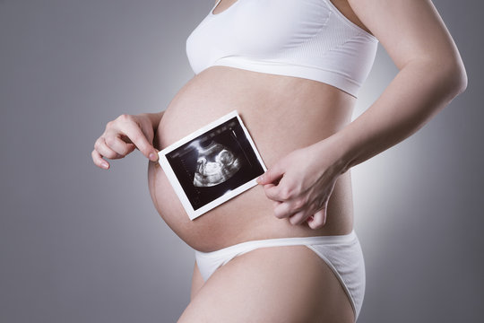 Pregnant woman in white underwear with baby ultrasound scan on gray background