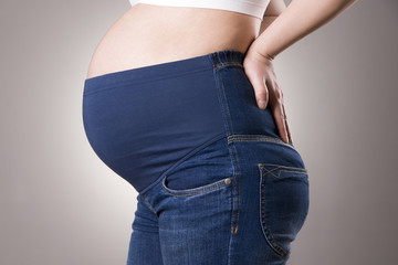Pregnant woman in blue jeans for pregnant women on gray background
