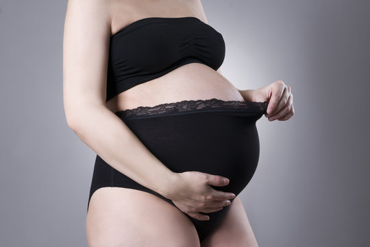 Pregnant woman in black supporting panties on gray background