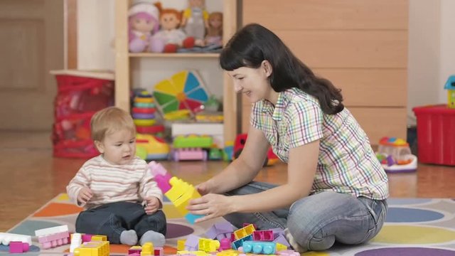Симпатичный маленький мальчик и мать, играя с игрушкой блоков дома, в комнате, сидя на полу.