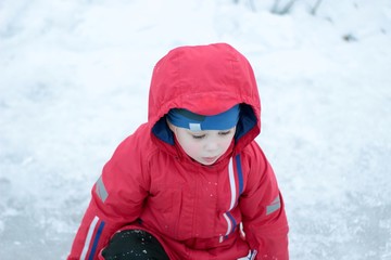 Fototapeta na wymiar Very sad cute little boy sits on snow.