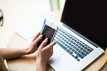 Close-up of female hands using smart phone while working on computer at modern office interior